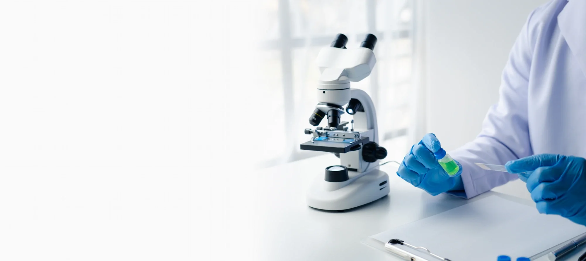 Analyst examining a sample vial beside a laboratory microscope