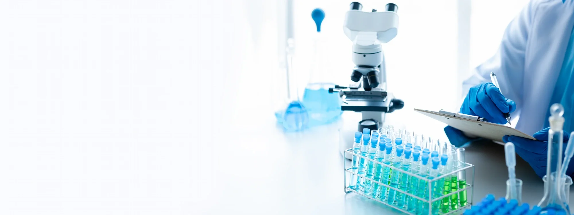 Analyst recording results beside a microscope and a rack of coloured test tubes