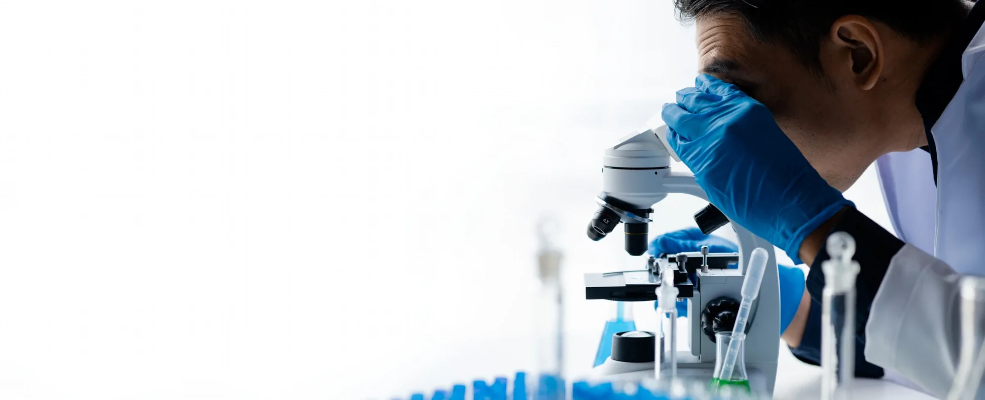Scientist examining a sample under a microscope beside a rack of blue test vials