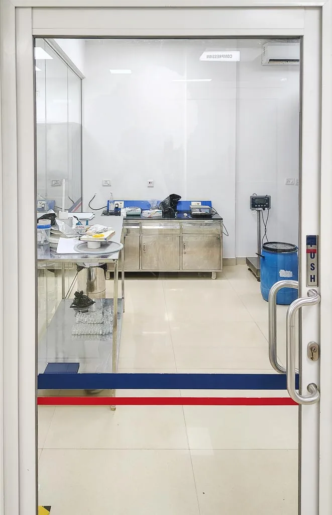 Compression in-process check station with weighing balances viewed through the cleanroom door at Stabicon